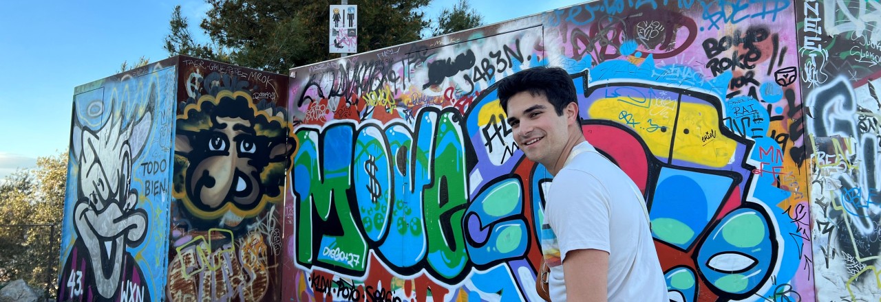 Study abroad sudent Ethan Arnone walks past a colorful wall of spray paint art.
